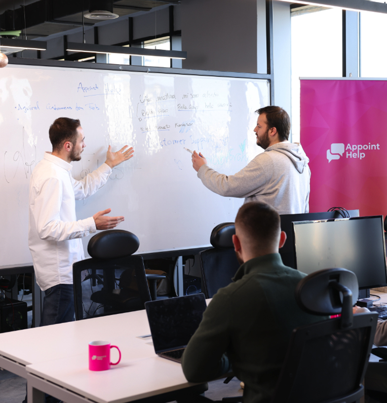 Two team members actively engaging in a strategic discussion in front of a whiteboard with notes and diagrams, in a well-lit office space.
