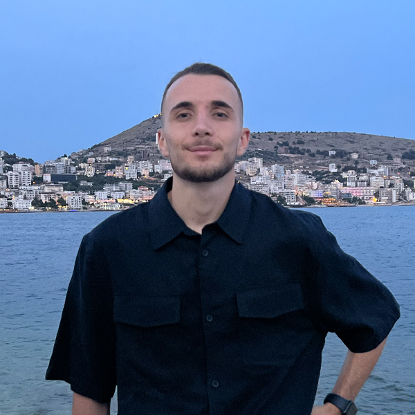 Confident young account manager in a dark shirt standing before a coastal cityscape at dusk, conveying professionalism and assurance.