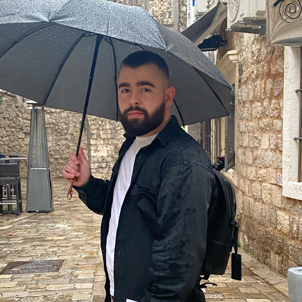 Website developer in a smart black jacket holding an umbrella, with an old stone street in the background, depicting readiness and adaptability.