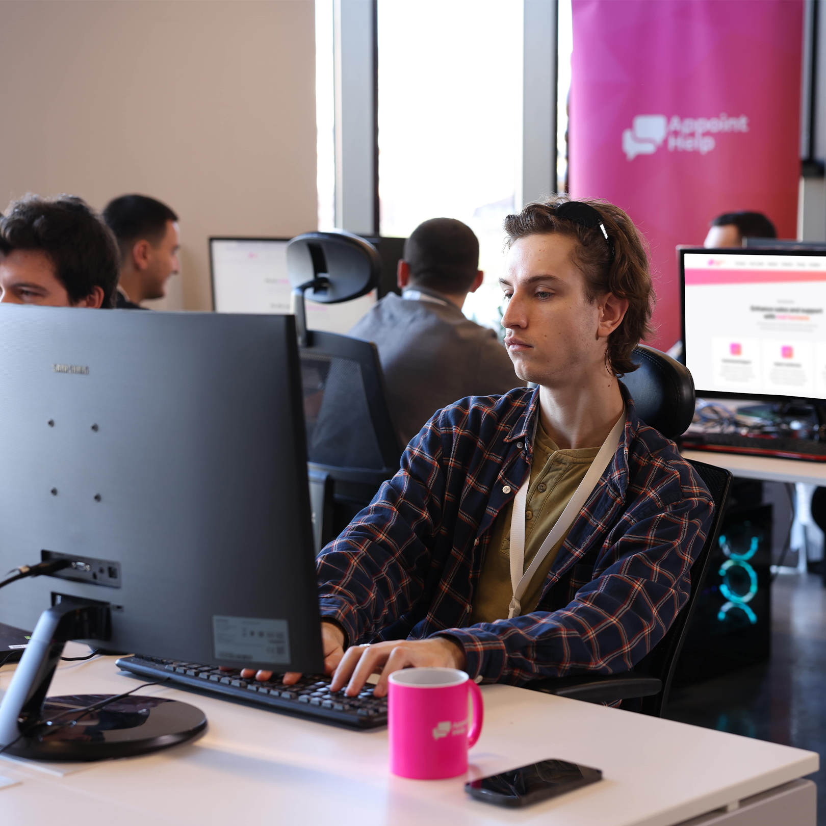 Focused customer service agent at work in a busy office environment, with a deep concentration on the computer screen and a branded mug on the desk.